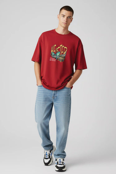 Red oversized graphic t-shirt with colorful "Heisted" text, paired with light blue jeans and sneakers.